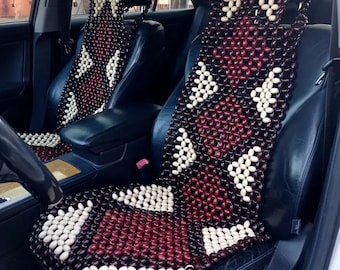 May include: Two brown and white beaded car seat cushions in a black leather car seat. The cushions are made of wooden beads and have a diamond pattern.