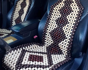 May include: A brown and white beaded car seat cushion. The cushion is made of wooden beads and has a diamond pattern. The cushion is in a car seat.