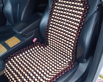 May include: A brown and beige wooden bead car seat cushion. The cushion is made of many small, round beads that are strung together in a grid pattern. The cushion is placed on a black leather car seat.