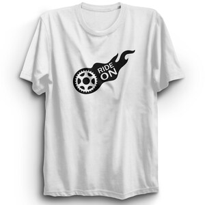 May include: White t-shirt with a black graphic. The graphic shows a gear and flames with the words "RIDE ON". The design is on the front of the shirt. The t-shirt has a crew neck and short sleeves.