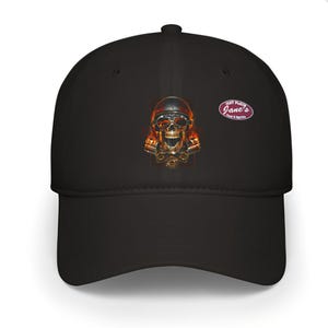 Op de afbeelding: Zwarte baseball cap met een schedelafbeelding met een bril en vlammen. De cap heeft een gebogen klep en een klein logo. Het schedelontwerp heeft gouden en oranje details. De cap is een klassieke stijl.