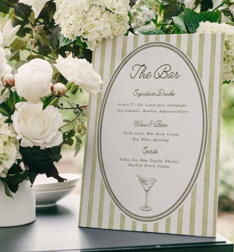 May include: A bar menu with a green and white striped design. The menu lists signature drinks, wine & beer, and spirits. White flowers and greenery surround the menu.