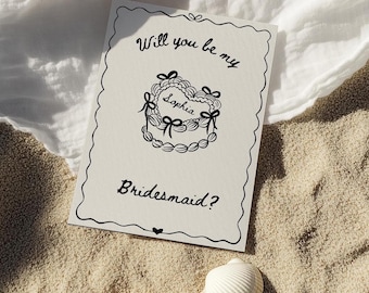 May include: A white card with black text and a simple illustration of a cake with the word "Sophia" on it. The text on the card reads "Will you be my Bridesmaid?"