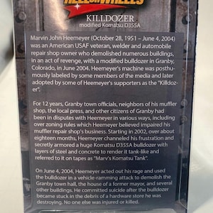 May include: A product box for the "Killdozer," a modified Komatsu D355A bulldozer. The box features text detailing the story of Marvin John Heemeyer, an American USAF veteran who demolished buildings in Granby, Colorado, in 2004.