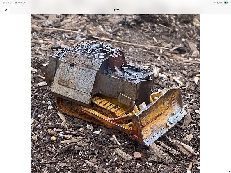 May include: A detailed model of a bulldozer, featuring a yellow blade and tracks, with a weathered, metallic finish. The model is set against a backdrop of wood chips and small debris, showcasing its construction and design.