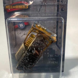 May include: A 1:87 HO scale model of the Killdozer, a modified Komatsu D355A bulldozer. The model is in a clear plastic package with the "HELLonWHEELS" logo and the text "TREAD ON THEM". The model is made in the USA.