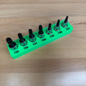May include: A set of Torx bit sockets in a bright green holder. The sockets are arranged in a row and labeled with sizes T27, T30, T40, T45, T47, T50, and T55. The tools are designed for use with a variety of fasteners.