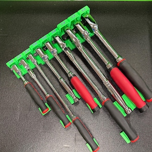 May include: A set of eight metal ratchets with black and red handles, organized in a bright green plastic storage rack. Each slot is labeled with size markings including 1/4, 3/8, and 1/2, indicating the drive size for each tool in the collection.