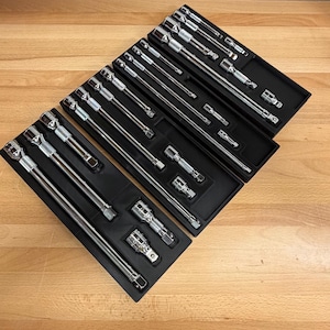 May include: A set of chrome-plated socket wrenches and extensions neatly arranged in black trays. The tools are displayed on a light brown wooden surface, showcasing their polished finish and various sizes. The set includes multiple sockets and extension bars.