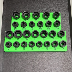 May include: A green socket organizer with black sockets of various sizes. The sockets are arranged in rows and columns, with sizes labeled in fractions and numbers. The organizer is on a dark surface.