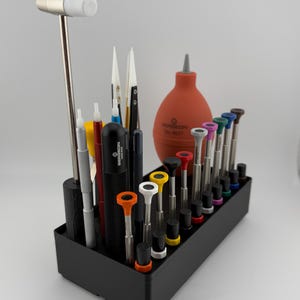 May include: A black tool organizer with a variety of tools, including screwdrivers, tweezers, and a rubber bulb air blower. The organizer has a white rubber mallet on the left side.