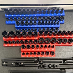 May include: A set of black socket wrenches organized in a blue and red tray. The wrenches are arranged by size, with the smallest wrenches on the left and the largest wrenches on the right. The tray has a variety of sizes, including 5/16, 3/8, 7/16, 1/2, 9/16, 11/16, 15/16, 1, 1-1/16, 1-3/16, 1-1/2, 1-5/8, 1-3/4, 2, 2-1/2, 2-3/4, 3, 3-1/2, 4, and 5. The tray also includes a black extension bar and a black socket wrench.
