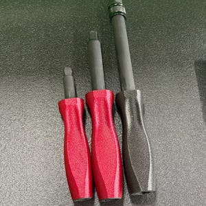 May include: Three screwdrivers with black shafts and textured handles. Two have red handles, and one has a black handle. The screwdrivers are of varying lengths, with the longest one featuring a knurled adjustment collar.