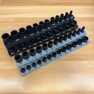 May include: Two socket organizers with various sized black sockets. The top organizer is black, and the bottom one is gray. The sockets are labeled with fractional inch measurements, ranging from 5/16 to 15/16.