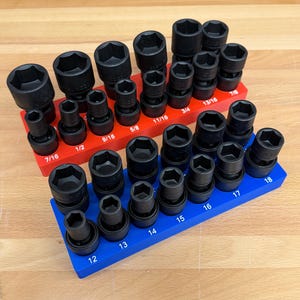 May include: A set of black impact sockets arranged on red and blue socket organizers. The sockets are various sizes, including 7/16, 1/2, 9/16, 5/8, 11/16, 3/4, 13/16, and 7/8 inch sizes. The blue organizer has sizes 12, 13, 14, 15, 16, 17, and 18.