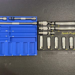 May include: A blue plastic tray with a variety of spark plug sockets. The tray has labels for different sizes of spark plugs. The sockets are arranged in a row on a black tray with the label "Spark Plugs".