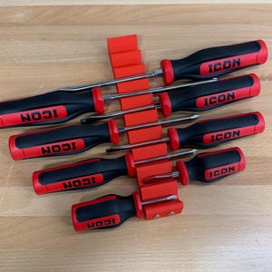 May include: A set of screwdrivers with black handles and red accents, featuring the word "ICON" in white. The screwdrivers are held in red plastic holders, arranged on a light brown wooden surface.