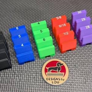 May include: A collection of colorful, stepped blocks labeled with numbers and fractions, ranging from 4 to 30. The blocks are black, blue, green, red, and purple. A round emblem with a dachshund and the text "DESIGNS by LOU" is also present.