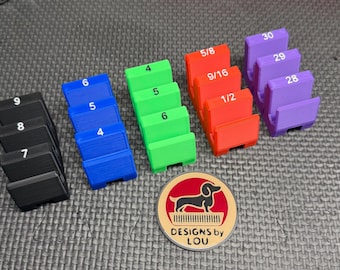 May include: A collection of colorful, stepped blocks labeled with numbers and fractions, ranging from 4 to 30. The blocks are black, blue, green, red, and purple. A round emblem with a dachshund and the text "DESIGNS by LOU" is also present.