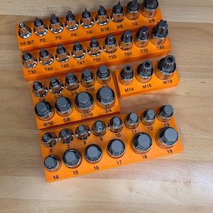 May include: A collection of metal socket and bit sets organized in bright orange plastic trays. The sets include various sizes labeled with imperial and metric markings such as 1/4 BIT, T80, M18, 3/4, and 19, featuring chrome and grey steel finishes.