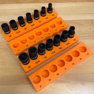 May include: An assortment of black impact sockets arranged on bright orange socket organizers. The sockets are labeled with fractional inch sizes, including 3/8, 7/16, 1/2, 9/16, 5/8, 11/16, 3/4, 13/16, and 7/8 inches. The organizers have numbered holes.
