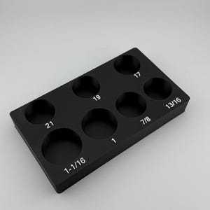 May include: Black plastic tray with seven round holes for storing different sized drill bits. The holes are labeled with the sizes: 1-1/16, 1, 7/8, 13/16, 19, 17, and 21.