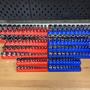 May include: A collection of chrome sockets arranged on red and blue socket organizers. The sockets are of various sizes, with measurements in inches clearly marked. The organizers are neatly displayed on a wooden surface, ideal for a workshop or garage.