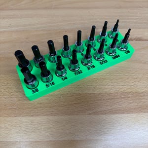 May include: A set of hex bit sockets in a bright green holder. The sockets are black with silver bases, and sizes are labeled in inches, including 3/8, 5/16, 1/4, 7/32, 3/16, 5/32, 9/64, and 1/8.