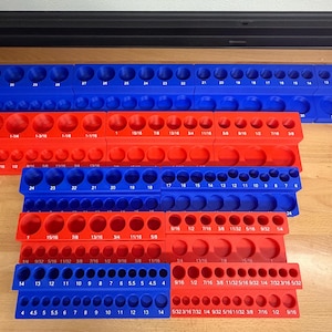 May include: A collection of blue and red socket organizers. The organizers are made of plastic and have various sized holes to hold sockets. The sizes are printed on the organizers in both fractions and numbers.