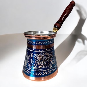 Puede incluir: Una cafetera turca tradicional con un acabado azul y cobre. La cafetera tiene un diseño floral decorativo y un mango de madera.