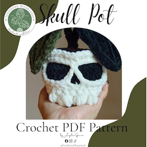 Op de afbeelding: Een wit en zwart gehaakte pot in de vorm van een schedel met donkergroene en zwarte gehaakte bladeren aan de bovenkant. De afbeelding bevat de tekst Skull Pot, Crocheted Botanicals en Crochet PDF Pattern by Angelica Spencer.