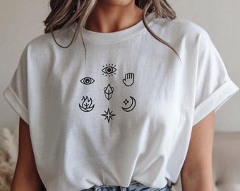 May include: White t-shirt featuring a collection of black line art symbols, including eyes, a hand, a flame, a crystal, a star, and a crescent moon. The shirt has rolled-up sleeves and a relaxed fit.