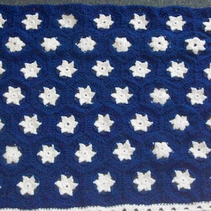 May include: A crocheted blanket in a design inspired by the American flag. The blanket features a blue field with white star motifs, a white border, and a red and white striped section. The blanket is made of yarn and is handmade.