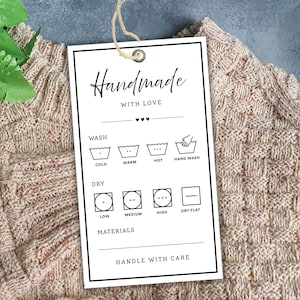以下が含まれることがあります： 「Handmade WITH LOVE」の文字が黒い筆記体で書かれた白いタグ。洗濯と乾燥の指示が下にあります。タグは、色の斑点のあるベージュ色のニット衣類に付いています。