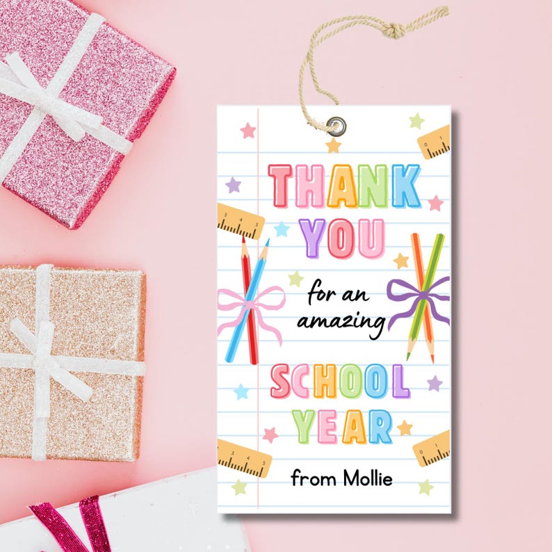 K&ouml;nnte beinhalten: Ein wei&szlig;es Geschenk-Etikett mit dem Text "THANK YOU for an amazing SCHOOL YEAR from Mollie." Das Etikett zeigt farbenfrohen Text, Bleistifte, Lineale und Sterne. Oben ist eine Schnur befestigt. Rosa und goldene Geschenkverpackungen sind im Hintergrund.