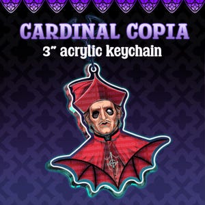 May include: A 3-inch acrylic keychain featuring an illustration of Cardinal Copia wearing a red ecclesiastical robe and hat, with a bat-wing design at the base. The text CARDINAL COPIA and 3 inch acrylic keychain are printed above the figure.