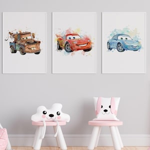 Könnte beinhalten: Drei gerahmte Aquarelldrucke mit Cartoon-Autos: ein rostiger Abschleppwagen, ein rotes Rennauto und ein blaues Auto. Die Drucke haben einen weißen Hintergrund und werden über zwei kleinen rosa und weißen Stühlen mit tierförmigen Kissen angezeigt.