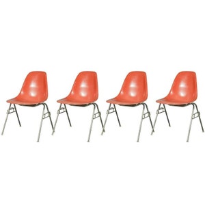 May include: Set of four vintage orange fiberglass chairs with metal legs. The chairs are arranged in a row.