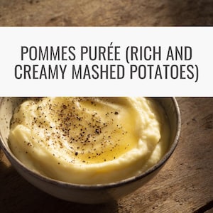 Op de afbeelding: Een kom romige aardappelpuree, gegarneerd met een scheutje boter en zwarte peper. De tekst "POMMES PURÉE (RIJKE EN ROMIGE AARDAPPELPUREE)" wordt boven de kom weergegeven. De kom staat op een houten oppervlak.