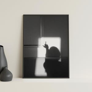 以下が含まれることがあります： 手でお粗末なジェスチャーをしている人の影の白黒写真。影は白い壁に映し出されています。