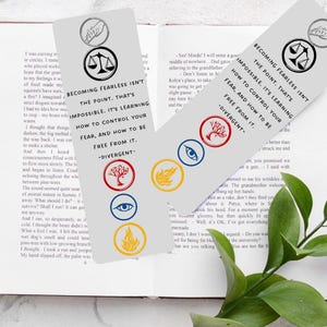May include: A set of five Divergent book bookmarks featuring the faction symbols: Abnegation, Amity, Candor, Dauntless, and Erudite. The bookmarks are printed on a gray background with white text. The text on the bookmarks reads: "Becoming fearless isn't the point. That's impossible. It's learning how to control your fear, and how to be free from it. -Divergent"