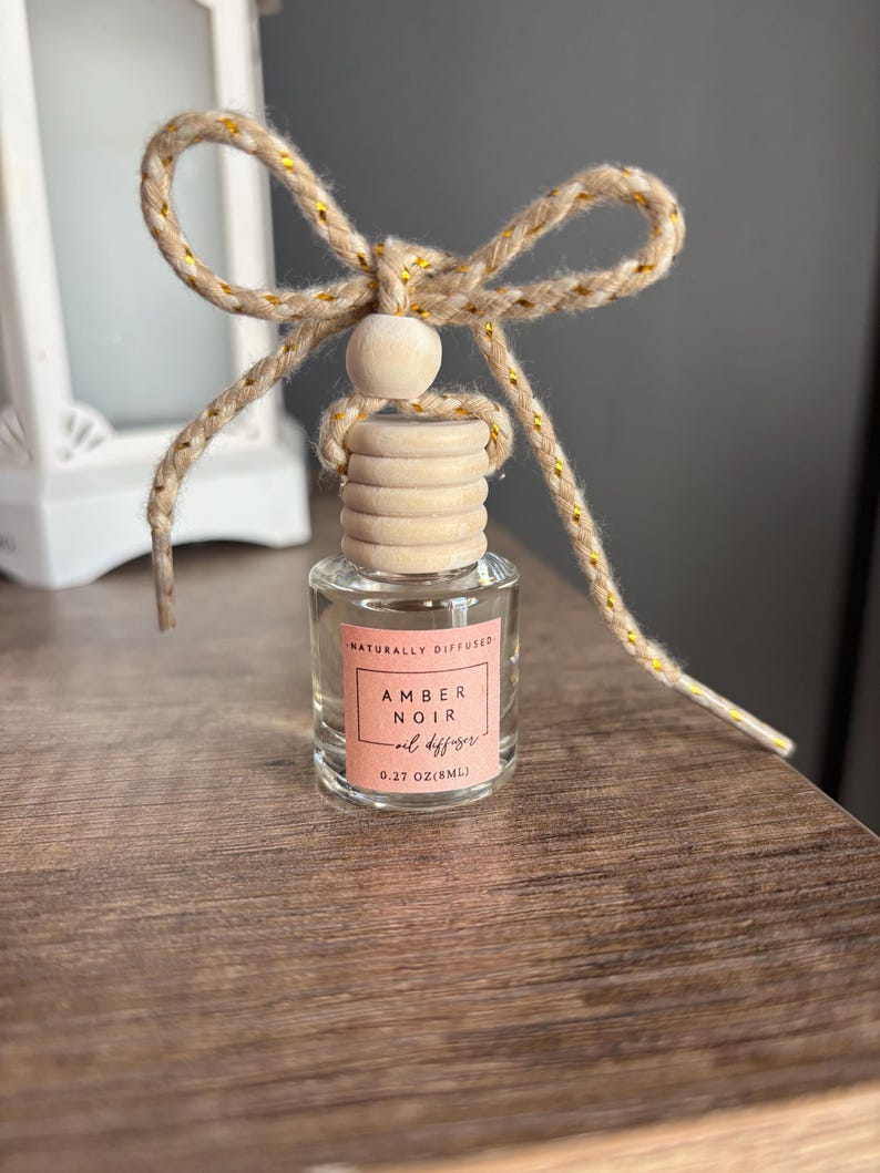 May include: A small glass bottle with a wooden cap and a natural twine bow. The bottle contains a natural oil diffuser labeled "Amber Noir oil diffuser 0.27 oz/8mL" and "Naturally Diffused".