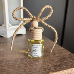 May include: A small glass bottle with a wooden cap and a natural twine bow. The bottle contains a clear liquid and has a label that reads "Naturally Diffused Neroli & White Jasmine Oil Diffuser 0.27 oz (8mL)"