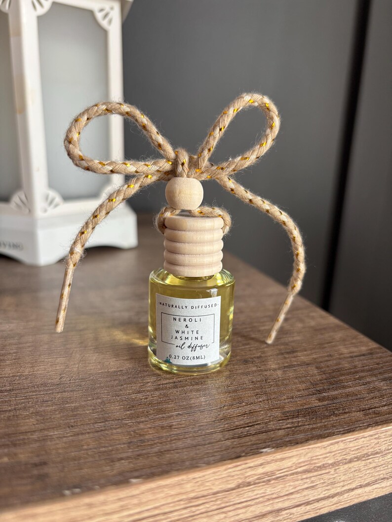 May include: A small glass bottle with a wooden cap and a natural twine bow. The bottle contains a clear liquid and has a label that reads "Naturally Diffused Neroli & White Jasmine Oil Diffuser 0.27 oz (8mL)"