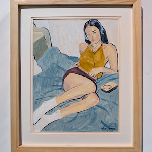 May include: A framed painting depicting a person with dark hair wearing blue headphones, a mustard yellow halter top, and a dark skirt. The person is reclining on a blue bedspread, wearing white socks, with a small rectangular device nearby.