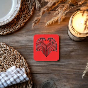 May include: Red square coaster with a black and white graphic of two eagles forming a heart shape.