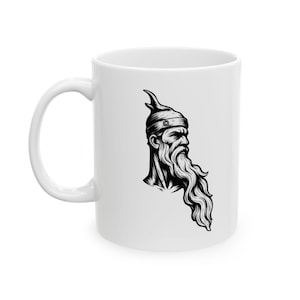 May include: White ceramic mug featuring a black and white illustration of a bearded man wearing a horned helmet. The design is a detailed, stylized portrait. The mug has a curved handle and a glossy finish.