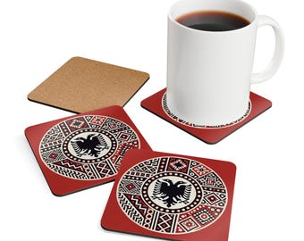 May include: A white ceramic mug with coffee sits on a red square coaster featuring a black double-headed eagle design. Additional coasters with the same design are visible, along with a plain cork coaster.
