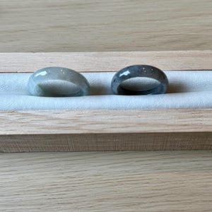 May include: Two jade rings, one light green and one dark green, displayed in a wooden box with a white velvet lining.