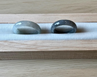 May include: Two jade rings, one light green and one dark green, displayed in a wooden box with a white velvet lining.